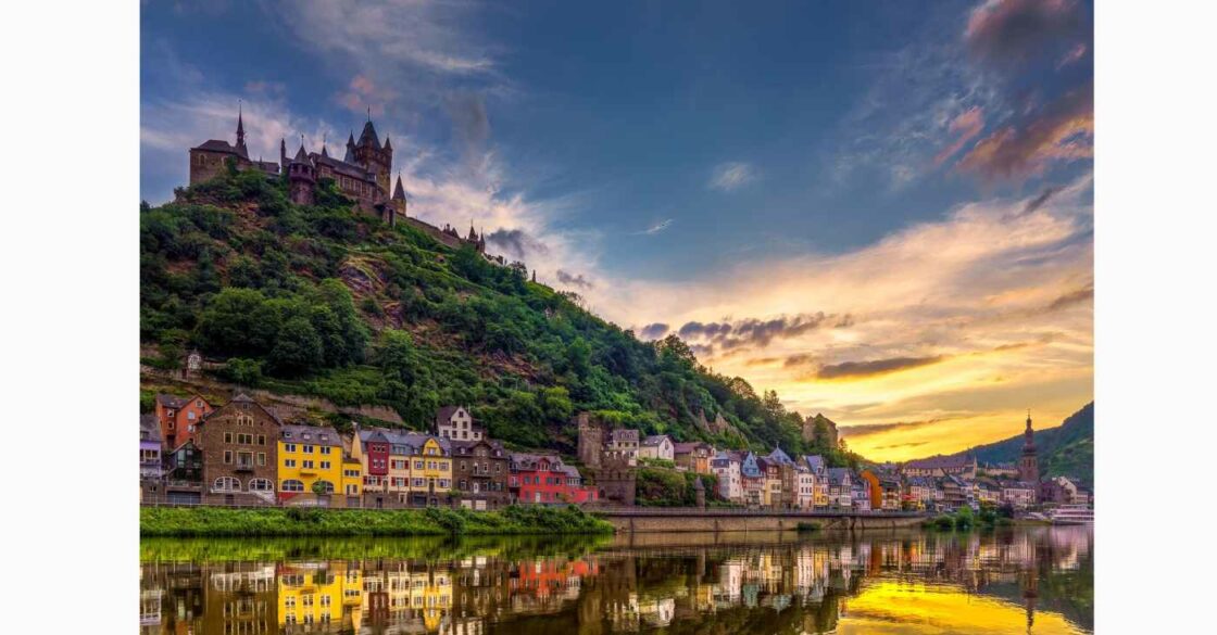 Sonnenuntergang an der Reichsburg Cochem und Wasserreflektion der farbigen Häuser am Ufer.